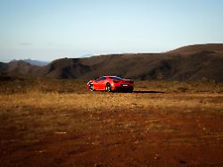 a bright red ferrari car parked on a lush green grass field with majestic mountains in the background