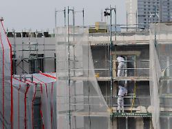 bauarbeiter verputzen eine gedaemmte fassade auf einer baustelle fuer frei finanzierte eigentumswohnungen im kfw40 qng standard