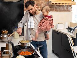 busy father looking after baby girl making meal and talking on mobile phone multitasking man at home in kitchenn