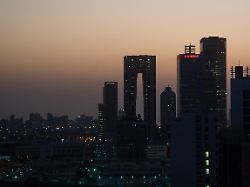 die aufgehende sonne faerbt den himmel hinter der skyline von kuwait city roetlich