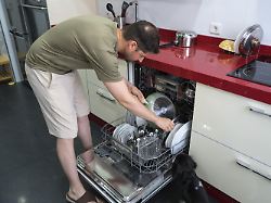 ein mann in freizeitkleidung laedt geschirr in eine spuelmaschine in einer modernen kueche