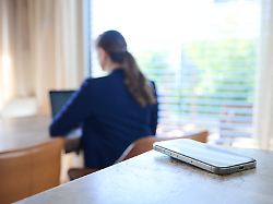 ein smartphone liegt auf einem tisch im hintergrund arbeitet eine frau an einem laptop