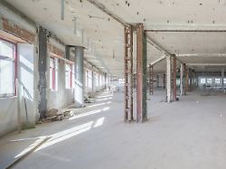 ein grosser leerer industrieraum mit freiliegenden balken und verstreuten baumaterialien