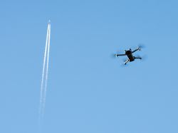 eine drohne fliegt im blauen himmel im hintergrund zieht ein passagierflugzeug kondensstreifen hinter sich her