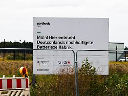 eine informationstafel steht vor der baustelle der geplanten batteriefabrik northvolt