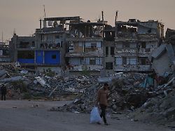 palaestinenser gehen im suedlichen gazastreifen eine strasse entlang die von gebaeuden umgeben ist die bei israelischen luft und bodenoperationen zerstoert wurden