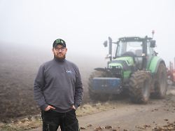 stefan leichenauer landwirt in tengen steht waehrend eines fototermins vor seinem schlepper neben einem gepfluegten acker