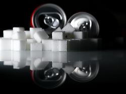 zwei getraenkedosen mit softdrinks und zahlreiche zuckerwuerfel liegen auf einem tisch