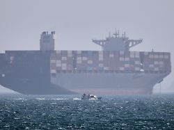 ein containerschiff liegt vor anker waehrend im vordergrund ein kleines motorboot in der strasse von hormus vor vorbeifaehrt 2