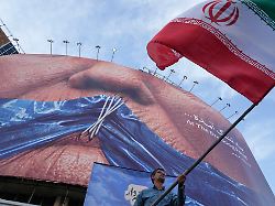 ein mann schwenkt bei einer regierungsnahen aktion eine iranische flagge vor einer plakatwand mit einer darstellung der strasse von hormuz und zugenaehten lippen von us praesident trump