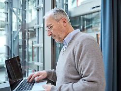 ein aelterer mann arbeitet konzentriert an einem laptop in einer modernen bueroumgebung