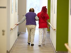 eine pflegekraft begleitet im drk pflegezentrum solferino eine seniorin durch den flur