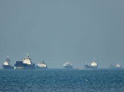 frachtschiffe darunter massengutfrachter und stueckgutfrachter liegen vor der kueste vor anker waehrend im vordergrund ein kleines motorboot in der strasse von hormuz vor bandar abbas iran vorbeifaehrt