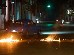 menschen fahren mit einem amerikanischen oldtimer durch eine barrikade die von anwohnern errichtet wurde die gegen anhaltende stromausfaelle in havanna protestieren
