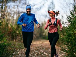 iling man and woman run together along a scenic forest trail on a cool day dressed in athletic gear enjoying nature fitness and each others company