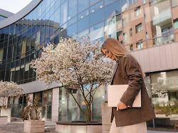 businesswoman walking with laptop outside modern office in spring model released symbolfoto vivf01871