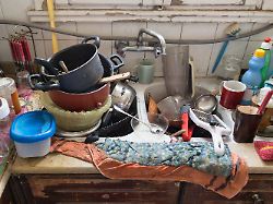 close up photo of a messy kitchen sink filled with dirty high piled dishes and utensils 1