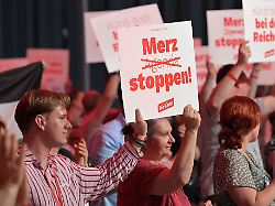 delegierte beim bundesparteitag der linken protestieren mit plakaten waehrend des parteitages in der metropolishalle gegen die politik von kanzler merz