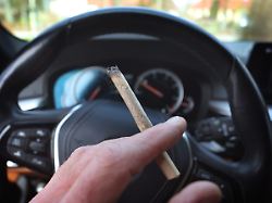 ein mann sitzt mit einem joint zwischen den fingern am steuer eines autos