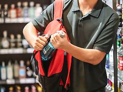 ein mann steckt in einem supermarkt eine flasche mit einem alkoholhaltigen getraenk in seinen rucksack