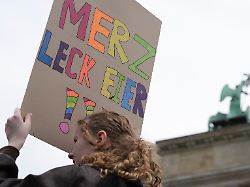 eine teilnehmerin einer demonstration haelt ein plakat auf dem steht merz leck eier menschen versammeln sich vor dem brandenburger tor in berlin um gegen die wehrpflicht zu demonstrieren