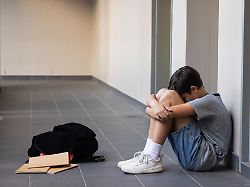 sitting in school hallway boy hugging knees with backpack and notebooks nearby