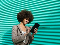 smiling woman browsing tablet outdoors by a turquoise wall model released symbolfoto egaf02621