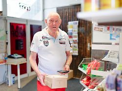 der 83 jaehrige christian lange haelt in seiner paketannahmestelle ein paket in den haenden