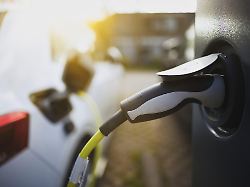 e auto mit ladekabel und stromstecker an einer ladesaeule angeschlossen bei sonnenaufgang im gegenlicht in einem wohngebiet an der strasse schagen nordholland niederlande