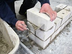 ein auszubildender im maurer handwerk nimmt in einem ausbildungszentrum mit der kelle den ueberstehenden moertel von der mauer die er im unterricht gebaut hat