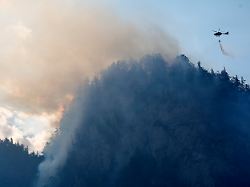 ein hubschrauber laesst zur bekaempfung eines brandes im bergwald in den chiemgauer alpen loeschwasser ab