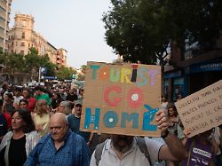 ein teilnehmer des protestzugs in palma haelt ein schild mit der aufschrift tourists go home waehrend einer demonstration gegen den tourismus auf mallorca