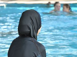 eine schuelerin sitzt in einem burkini am rande eines schwimmbeckens