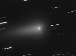 in der mitte ist der komet 3i atlas zu sehen die sterne im hintergrund erscheinen als lichtspuren weil die aufnahme aus mehreren nacheinander aufgenommen einzelbildern zusammengesetzt wurde
