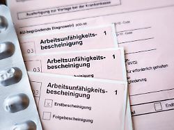 mehrere formulare zur arbeitsunfaehigkeitsbescheinigung liegen neben einem blister mit tabletten auf einem tisch