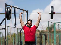 middle eastern arab man performs an overhead barbell lift in an open air crossfit gym demonstrating strength focus and determination during a high intensity outdoor workout session