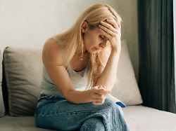 upset sad woman holding pregnancy test while sitting on sofa at home
