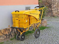 abgestellter gelber transportwagen zum austragen und verteilen von zeitungen und analoger post deutsche post