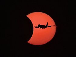 ein flugzeug vom typ boeing 747 fliegt waehrend der partiellen sonnenfinsternis vor der teilweise vom mond verdeckten sonne