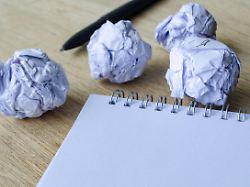 ein schreibtischarrangement mit mehreren zerknitterten papierstuecken und einem leeren notizblock das frustration kreativen kampf und den prozess der verfeinerung von ideen vermittelt