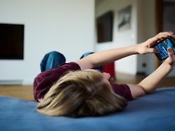 ein teenager guckt auf ein handy waehrend er auf einer matratze liegt