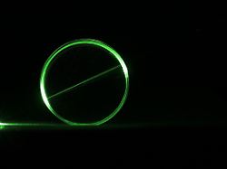 ein gruener laserstrahl durchbricht ein rundes glasprisma