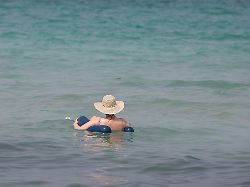 eine person entspannt sich am strand von can picafort und schwimmt mit einem sonnenhut auf dem kopf im wasser an der nordkueste von mallorca