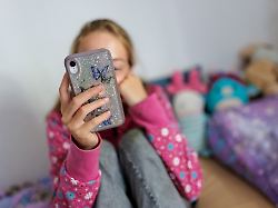 symbolfoto zum thema handynutzung bei kindern ein maedchen sitzt in ihrem bett und ist am handy berlin 22 07 2025