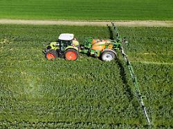 themenfoto landwirtschaft duengen pestizide ein landwirt faehrt mit seinenm traktor ueber ein gruenes feld und duengt mit pestiziden